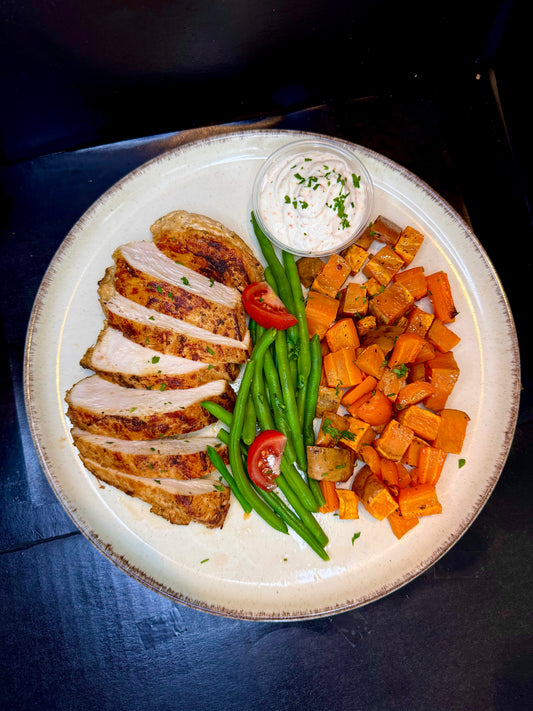 Plated dish with sliced chicken, green beans, carrots, and a side of sauce on a dark surface.